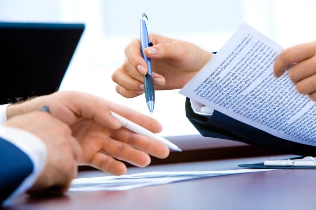 A person holding a pen and paper while another holds a pen.