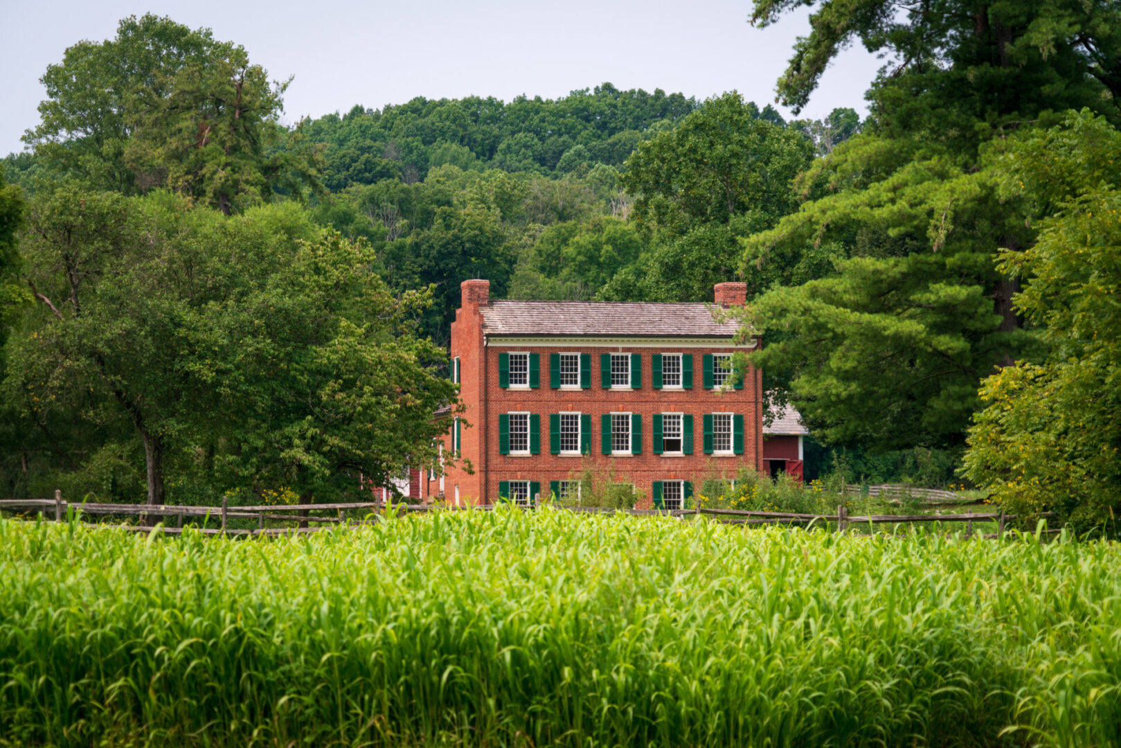 A brick house with green shutters in the middle of a field.